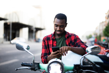 Handsome African man with scooter in the city. Young man using the phone..