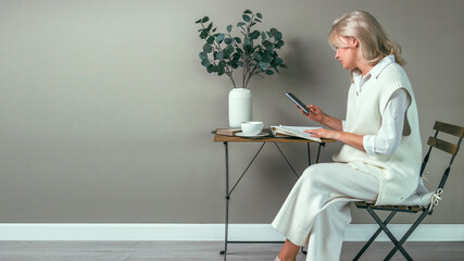 A young girl sits at a coffee table with a phone in her hands, distracted from the book. Side view.