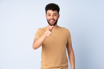 Young Moroccan man isolated on blue background surprised and pointing front