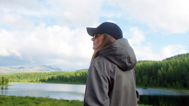 A girl with glasses opens the pocket of a gray anorak against the backdrop of a landscape