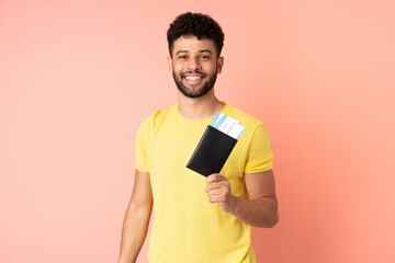 Young Moroccan man isolated on pink background happy in vacation with passport and plane tickets