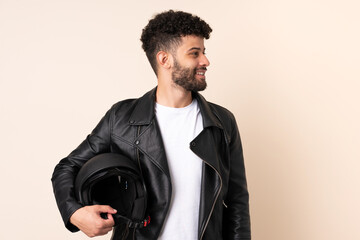 Young Moroccan man with a motorcycle helmet isolated on beige background looking side