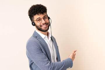 Telemarketer Moroccan man working with a headset isolated on beige background pointing back
