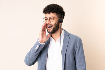 Telemarketer Moroccan man working with a headset isolated on beige background shouting with mouth wide open to the side