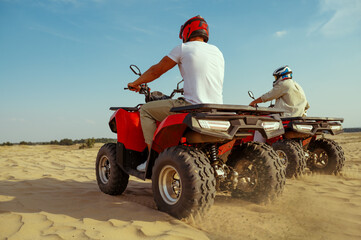 Obraz premium Two men in helmets riding on atv in desert sands
