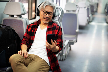 Senior man traveling by train. Man listening the music while enjoying in travel...