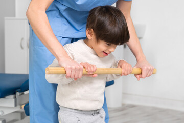 Physiotherapist and kid walking in rehabilitation center. Doctor supports a children with cerebral...
