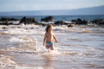 Fototapeta na wymiar Happy little child running on the tropical beach. Boy playing sea waves on vacation sea in the summer holiday. Kid in nature at seashore. Children walking at seaside.