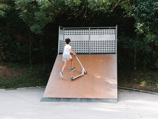 Little boy with scooter climbing on skate ramp in park
