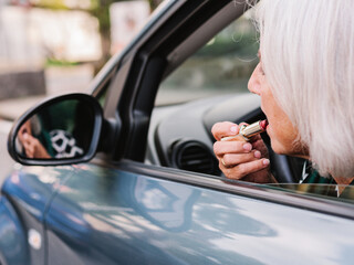 Senior elegant dressed woman making up lips on driver seat