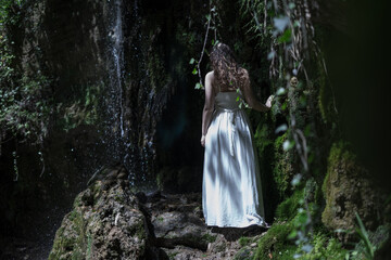 Beautiful model with wavy hairs in white dress near Castel Rinaldi waterfall under the moonlight,...