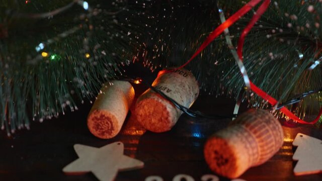 Happy New Year 2022. The camera moves from the top of the Christmas tree with cones, garlands and glitter to its base, where the wooden Christmas tree, snowflake, champagne corks and the numbers 2022