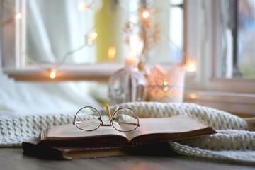 Open book and reading glasses. Candles and fairy lights in the background. Selective focus.