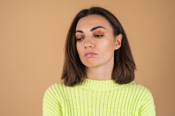 Fototapeta premium Young woman in a light green sweater on a beige background cute upset with a sad look, disappointed
