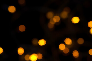 Defocused bokeh lights on black background, an abstract naturally blurred backdrop for Christmas eve or birthday party. Festive light texture. Yellow and red garland in blur. Overlay effect for design