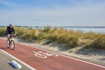 Bicycle path in the Netherlands. Dune with grass in front of a blue sea.1 male bicyclist motion...