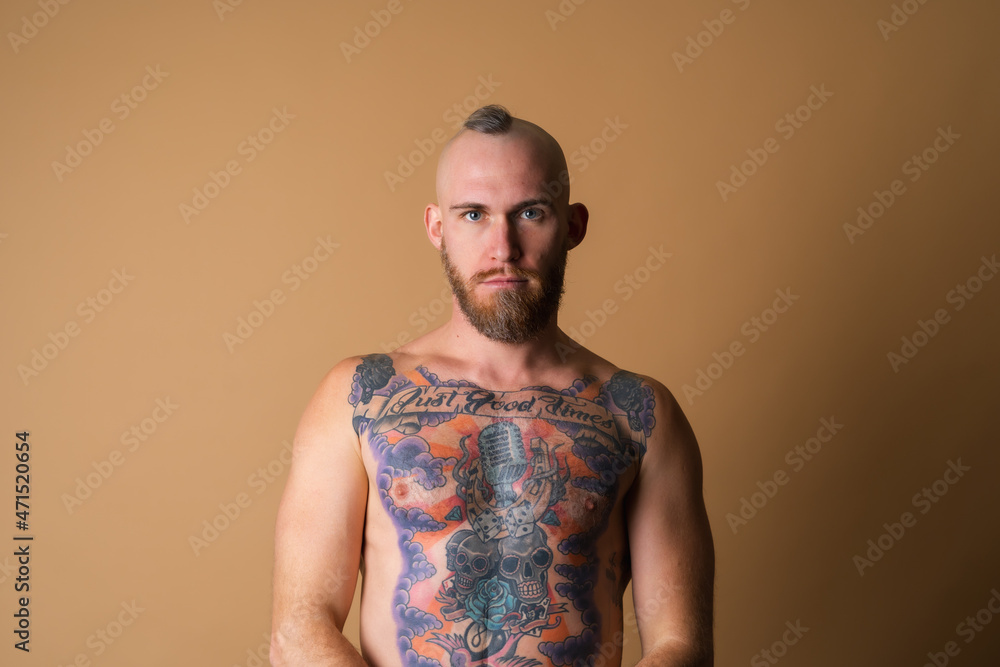 Wall mural tattooed brutal man with beard, topless naked on beige background, muscular with abs