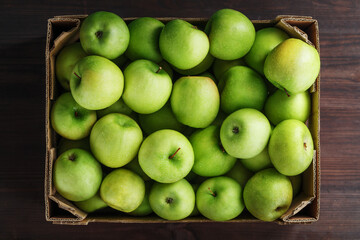 Ripe and juicy Green apples in a box on a wooden table.
