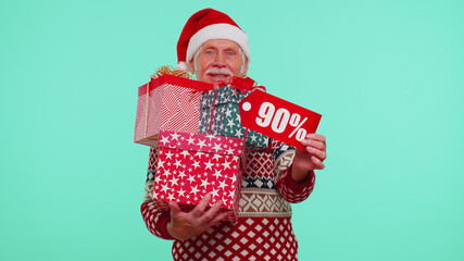 Senior grandfather man in Christmas sweater showing gift box and 90 Percent discount inscriptions banner text. Black Friday. Good holiday low prices for shopping. Blue studio wall background. New Year