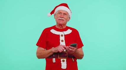 Elderly old grandfather man in Christmas red t-shirt looking smartphone display sincerely rejoicing...
