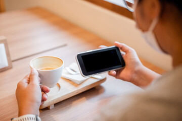 Woman enjoy drinking hot coffee while watching something on the mobile phone, isolated white screen on the phone as copy space