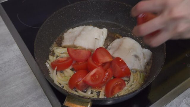 Female Hand lays vegetables to frying with fillet of sea codfish on frying pan. Appetizing and delicious dish closeup