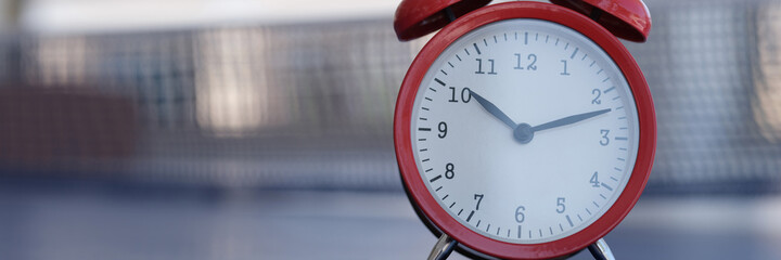 Red alarm clock standing on tennis table closeup