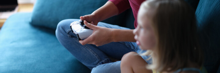 Mother and daughter sitting on couch and playing computer game with joystick closeup © H_Ko