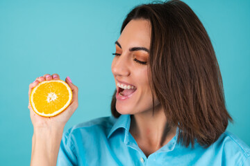 Young woman in a blue shirt on the background holds an orange, poses cheerfully, in high spirits, laughs smiles