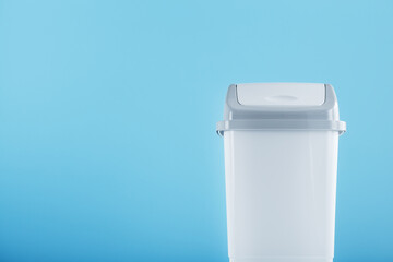White trash can on a light blue background with free space.