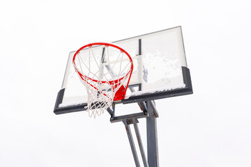 Red basketball hoop on a backboard on a light background, bottom view. Sports equipment for a team outdoor ball game. Steel frame, plexiglass shield.