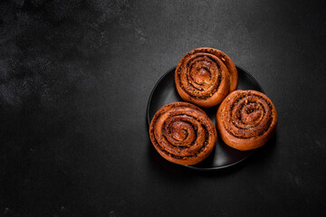 Freshly baked cinnamon roll with spices and cocoa filling on a black background