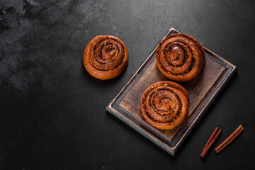 Freshly baked cinnamon roll with spices and cocoa filling on a black background