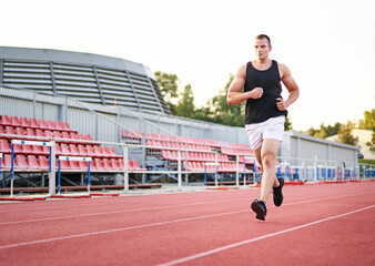 Fototapeta premium Young muscular fit male sprinter running on a red running track - Fitness and wellness concept with a millennial runner - Copyspace on the photo's left side