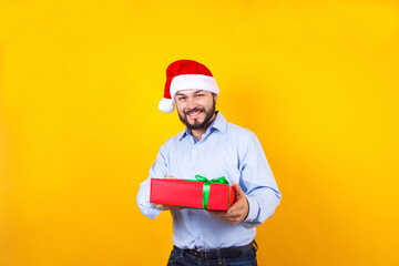 Portrait of young Latin man holding Christmas gift box on a yellow background in Mexico Latin America