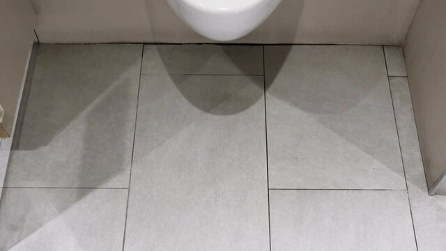 A white urinal in a public toilet. Point of view.