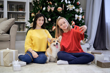 two teen girls Smiling making selfie photo together with a small dog corgi. Merry Christmas and Happy New Year. Christmas celebration.