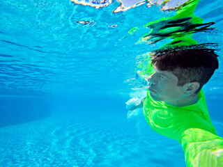Obraz na płótnie Canvas DCIM\100GUnderwater frontal view of a man in lime green t-shirt swimming in turquoise pool OPRO\G0080340.JPG