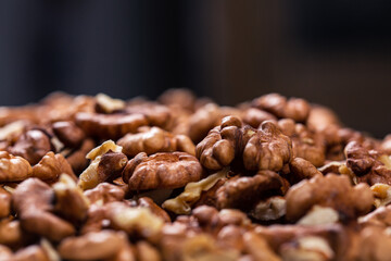 Heap of pieces of peeled textured walnuts against dark background.