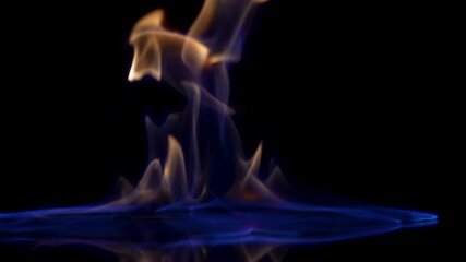 Falling match causes flames to ignite against black studio background. Combustion flammable liquid close up. Spot of gasoline ignites with flash and burns with blue yellow light in dark in slow motion
