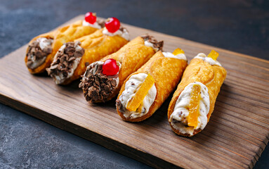 Traditional Italian Sicilian pastry dessert cannoli with creamy ricotta filling, chocolate crisps and fresh currant fruit served as close-up on a wooden design board - obrazy, fototapety, plakaty