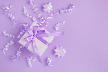 Gift box with tied purple bow and confetti on the puple background. Top view.Copy space.