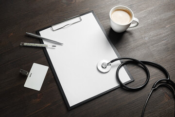 Medical still life. Blank clipboard, stethoscope, badge, thermometer, pen and coffee cup on wood table background.