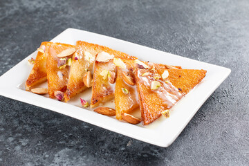 Shahi tukda or Double ka meetha is a bread pudding in ghee, garnish with Condensed Milk, Nuts & Mawa/khoya. Popular Indian Dessert, Served in a plate. Selective focus