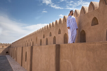omani man in traditional outfit walking on a wall of Jibreen castle