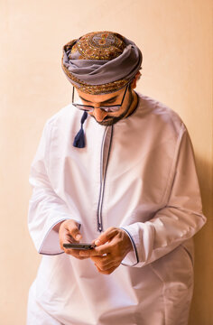 omani man in traditional outfit checking his mobile ohone