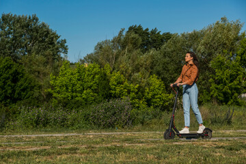 Naklejka na ściany i meble A young girl is driving on an electric scooter through the park