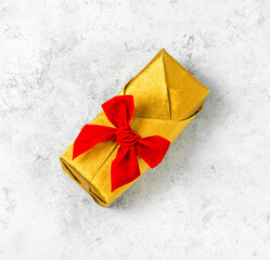 Gift box in gold paper with a red bow on a light gray background.