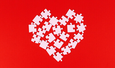 Heart made of white puzzle pieces on a red background