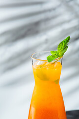 peach lemonade jug decorated mint leaf closeup. Summer cold drinks: homemade peach ice tea with ice cubes, and mint in glass on light background with shadow of tropic branch.